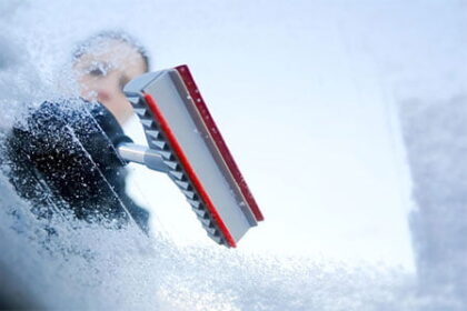 Woman cleaning ice from windshield to stay safe during winter driving months.