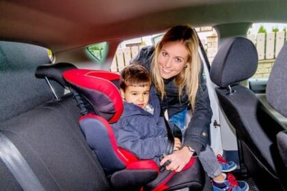 Woman strapping small child into car seat in backseat of automobile.