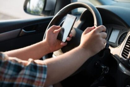 Male driver with cell phone in hand texting while operating a motor vehicle.