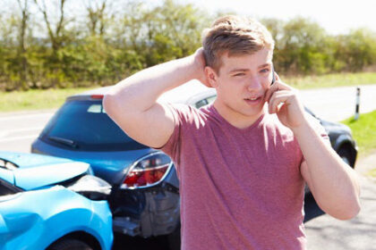 Young man talking on cell phone after a car accident.